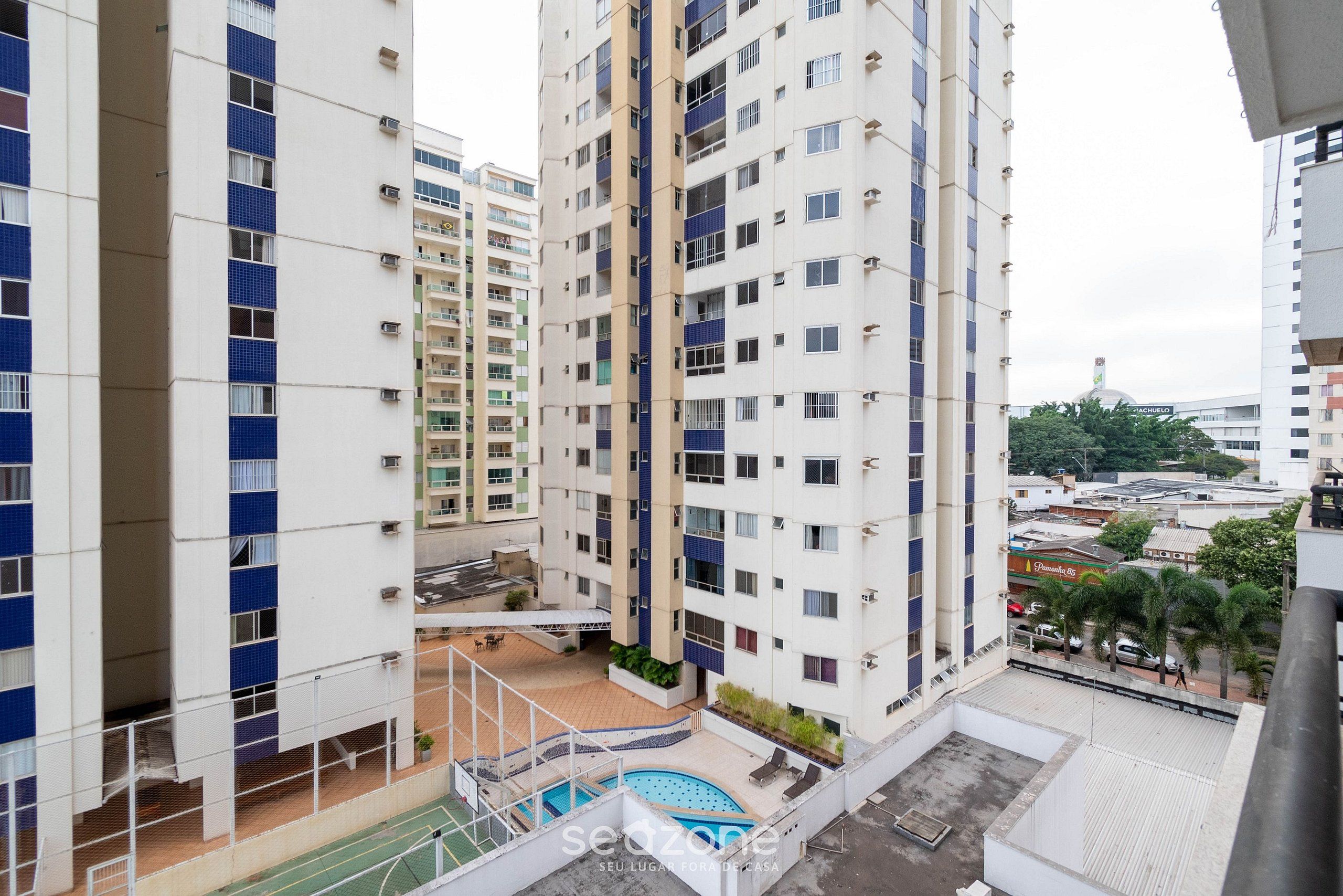 A high-rise residential building with multiple balconies, a rooftop pool, and a view of the surrounding cityscape.