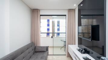 Una sala de estar moderna con un sofá gris, un televisor de pantalla plana montado en la pared y un balcón con puerta de vidrio.