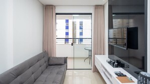 A modern living room with a grey sofa, a flat-screen TV mounted on the wall, and a balcony with a glass door. - Apartment Next to Flamboyant Shopping Mall - ESS (Goiânia)