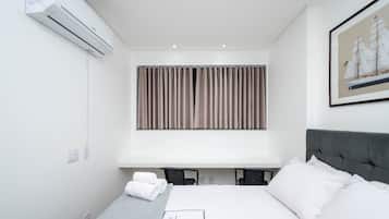 A modern hotel room with a large bed, a headboard, a window with curtains, an air conditioning unit, and a framed picture on the wall.