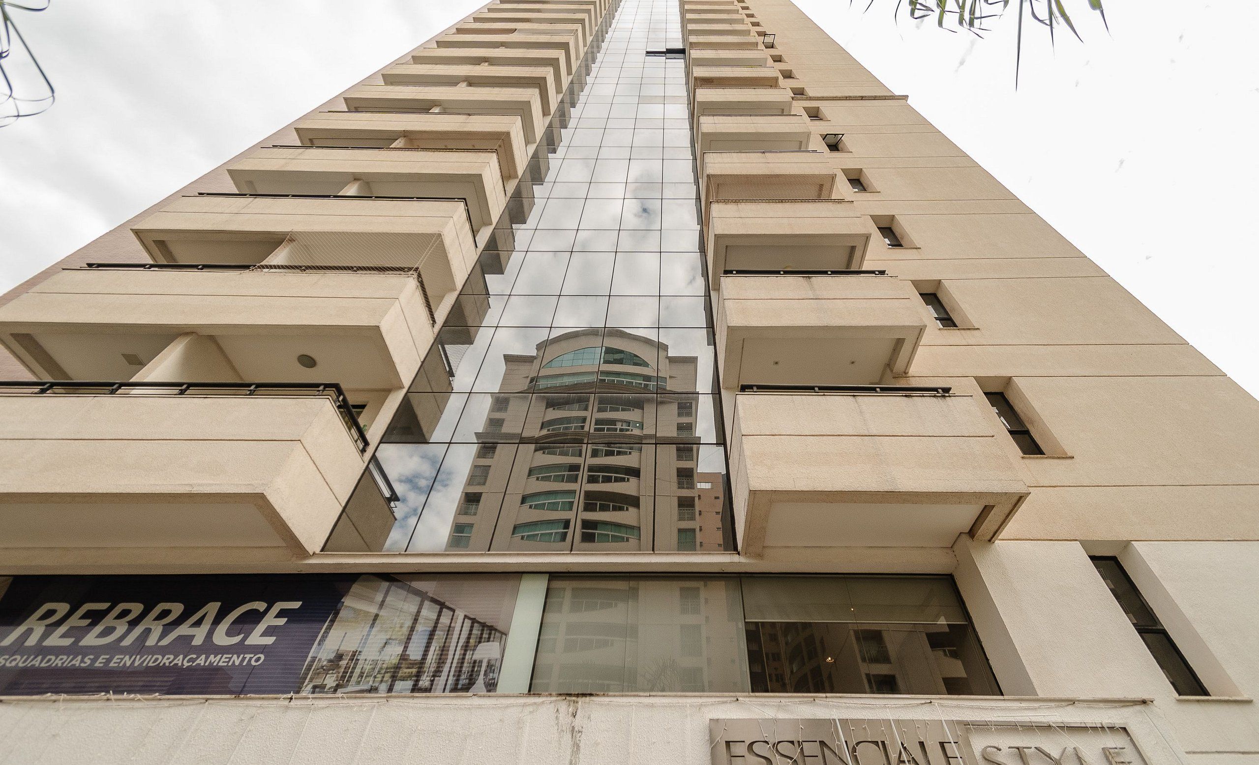 A tall building with a reflective glass facade and a sign reading "REBRACE SQUADRIAS E ENVIDRAÇAMENTO" at the bottom.