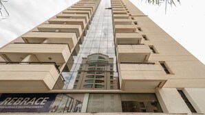 A tall building with a reflective glass facade and a sign reading "REBRACE SQUADRIAS E ENVIDRAÇAMENTO" at the bottom. - Apartment Next to Flamboyant Shopping Mall - ESS (Goiânia)