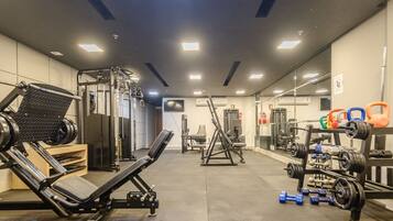 Un gimnasio con varios equipos de ejercicio, incluyendo una prensa de banca, una estructura para sentadillas y un banco de pesas.