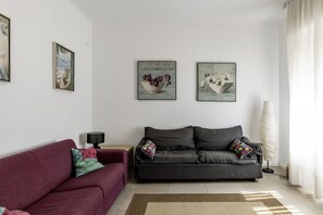 A living room with a dark grey sofa, a red sofa, and two wall-mounted paintings.