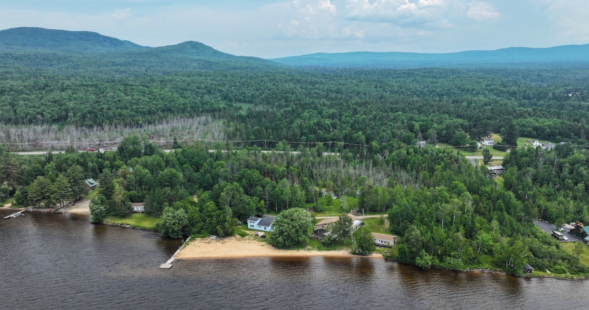 An aerial view of a lakeside property with multiple houses, a dock, and a forested landscape.