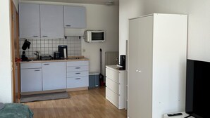 Ett kompakt boendeutrymme med ett litet kök, en platt-TV och en soffa.