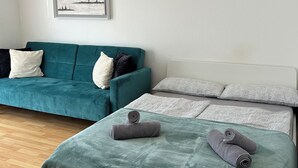 Ett modernt rum med en turkosfärgad soffa, en säng med ett grönt överkast och en inramad tavla på väggen.