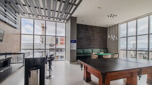 Un salón moderno con mesa de billar, asientos y ventanas amplias con vista a la ciudad.