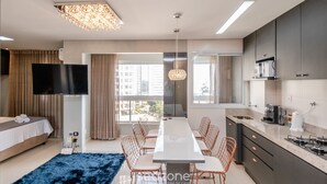 Una habitación de hotel moderna con una cama grande, una mesa de comedor con sillas, un área de cocina y un televisor montado en la pared.
