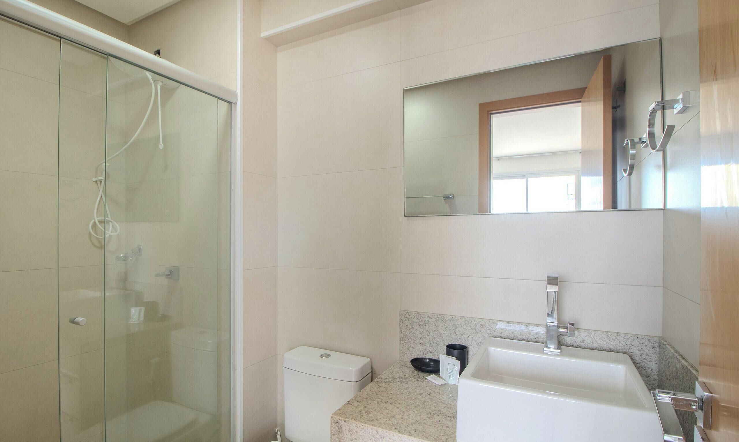 A bathroom with a glass shower enclosure, a white toilet, a sink with a mirror above it, and a granite countertop.