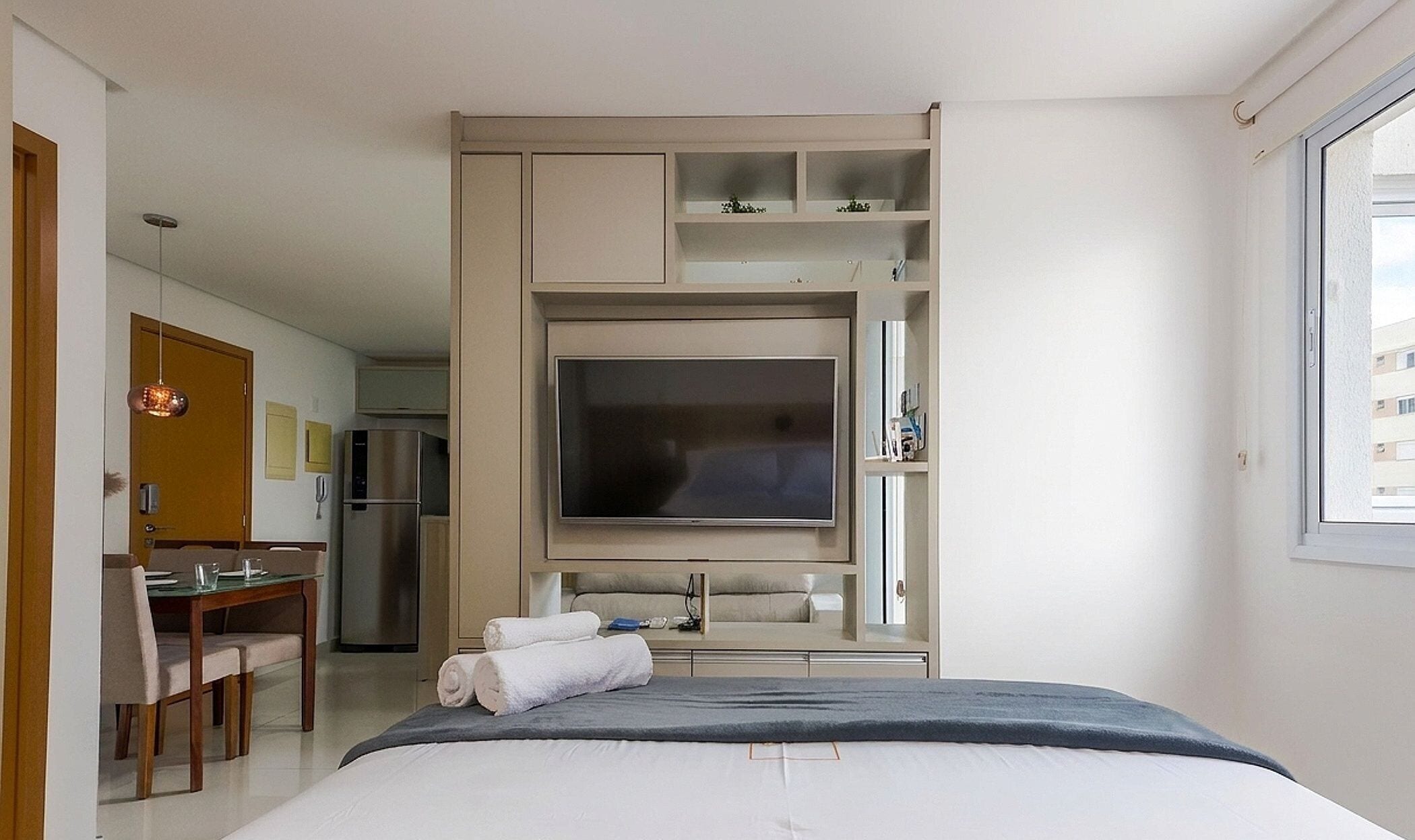 A hotel room with a bed, a TV, a desk with a chair, and a kitchenette area.