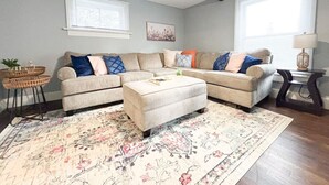 Ein Wohnzimmer mit Ecksofa, Hocker und einem gemusterten Teppich.
