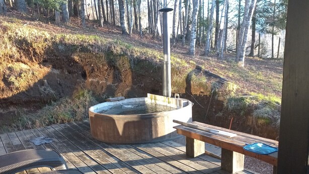 Eine Holzterrasse mit Whirlpool, Liegestühlen und Blick auf einen Wald.