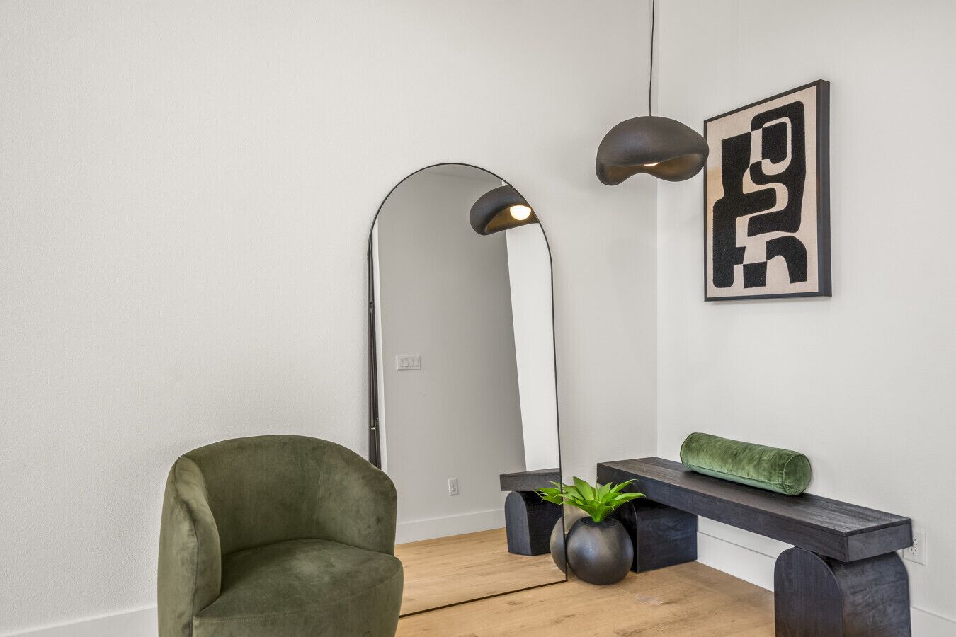 A modern living room with a green armchair, a tall floor lamp, a minimalist bench, and a framed abstract artwork.