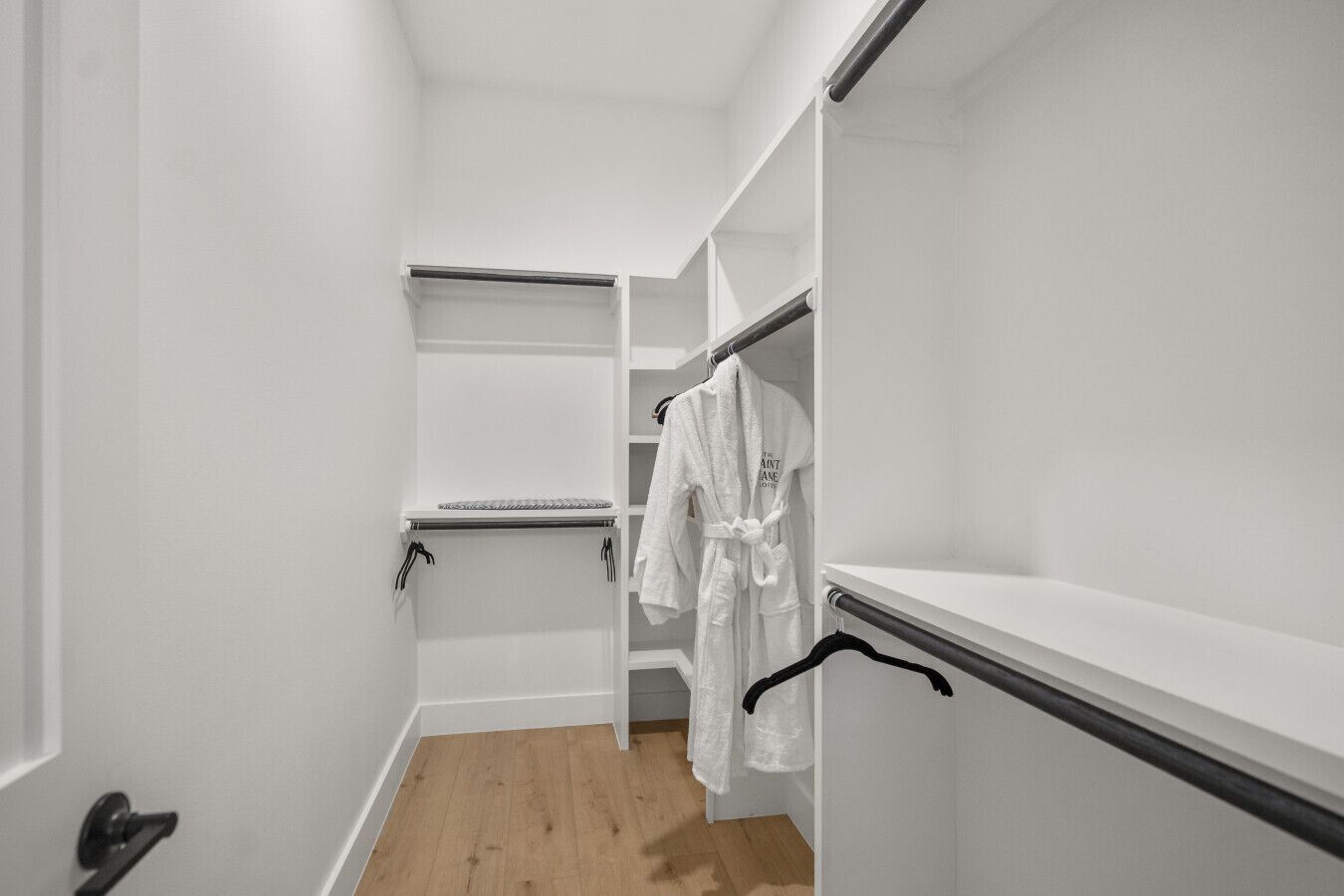 Um closet amplo com prateleiras abertas, roupeiro e piso de madeira.