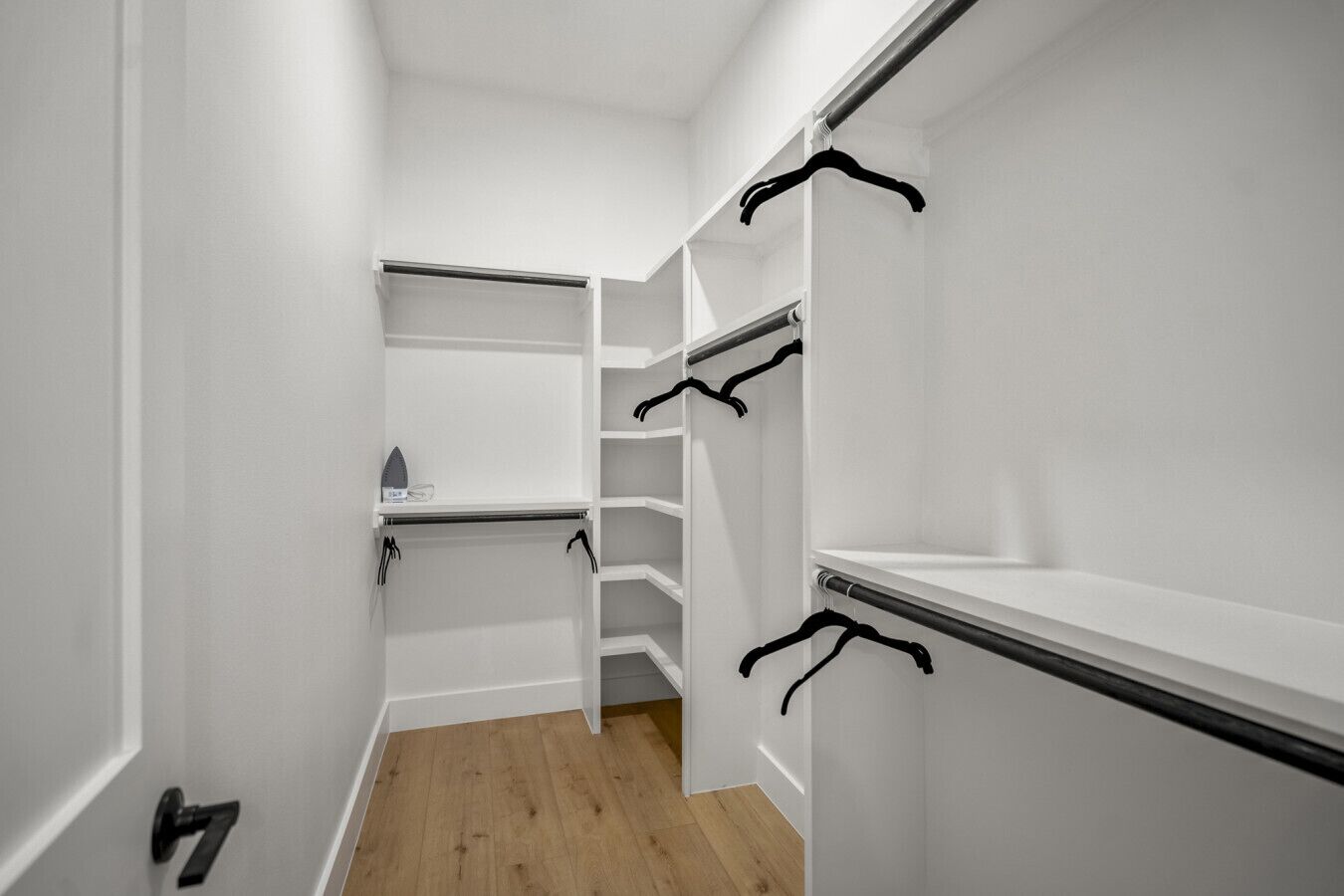 A walk-in closet with open shelves and hanging rods, a wooden floor, and a door with a number.