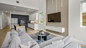 Ein modernes Wohnzimmer mit einem grauen Sofa, einem Couchtisch und einem an einer Holzwand befestigten Fernseher.