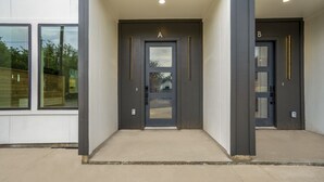 Ein moderner Gebäudeeingang mit zwei Türen, die mit A und B beschriftet sind, einem Betonweg und einer weißen Wand mit Fenstern.