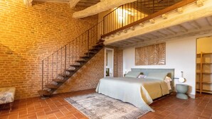 A bedroom with a brick wall, a wooden staircase, a bed with a headboard, and a nightstand.