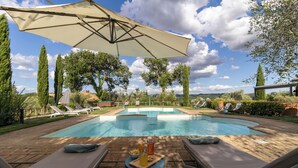 A poolside area with lounge chairs, a table with drinks, and a large umbrella providing shade.