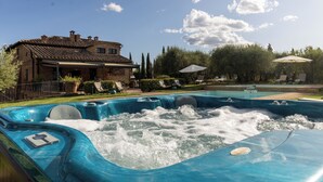 A swimming pool with hot tubs, lounge chairs, and a house in the background.