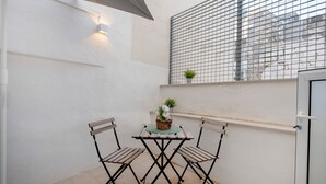 Een klein buiten zitgedeelte met een tafel, stoelen, een bloempot en een raam met metalen spijlen.
