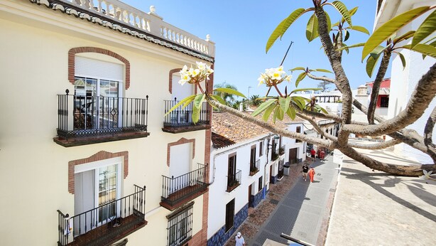 A narrow street with buildings featuring balconies and a clear blue sky. - CARABEO CASA PEPA (Nerja)