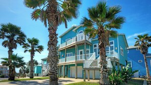 A two-story building with a balcony, surrounded by palm trees. - Sleeps 24 2 Homes w/ Beach Boardwalk Access & Deck Views Steps to the Beach (Port Aransas)