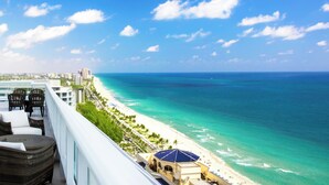 A balcony with wicker furniture overlooking a beach and ocean. - Luxurious Oceanfront Apartment in Fort Lauderdale (Fort Lauderdale Bea)