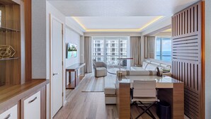 A modern hotel room with a wooden desk, a sofa, a TV, and a large window offering a view of the sea. - Luxurious Oceanfront Apartment in Fort Lauderdale (Fort Lauderdale Bea)