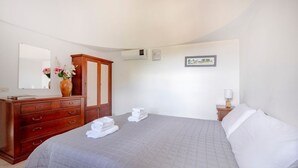 Um quarto com cama, cômoda, espelho, quadro e um vaso com flores.