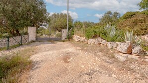 A gravel path leading to a gated entrance with a stone wall and a metal gate.