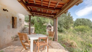 A covered outdoor dining area with stone flooring, wooden chairs, and a table.