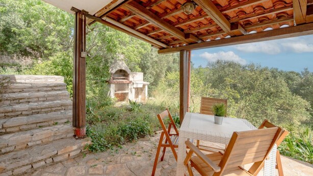 A covered outdoor seating area with stone steps, a grill, and a view of the surrounding greenery.