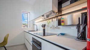 A modern kitchen with a built-in oven, a stainless steel range hood, and a window with a view of the outdoors. - GuestHost - Elegant Beachfront Wi-Fi & Parking (Golfo Aranci)