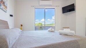 A hotel room with a bed, a TV mounted on the wall, a balcony with a view, and a towel rack. - GuestHost - Elegant Beachfront Wi-Fi & Parking (Golfo Aranci)