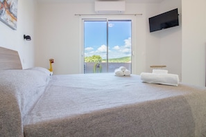 A hotel room with a bed, a TV mounted on the wall, a balcony with a view, and a towel rack.