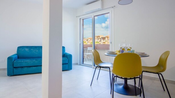A modern apartment with a dining area, two sofas, and a balcony with a city view. - GuestHost - Elegant Beachfront Wi-Fi & Parking (Golfo Aranci)