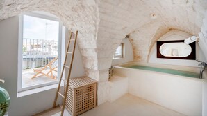 Un baño con bañera, ventana y vista a un edificio.