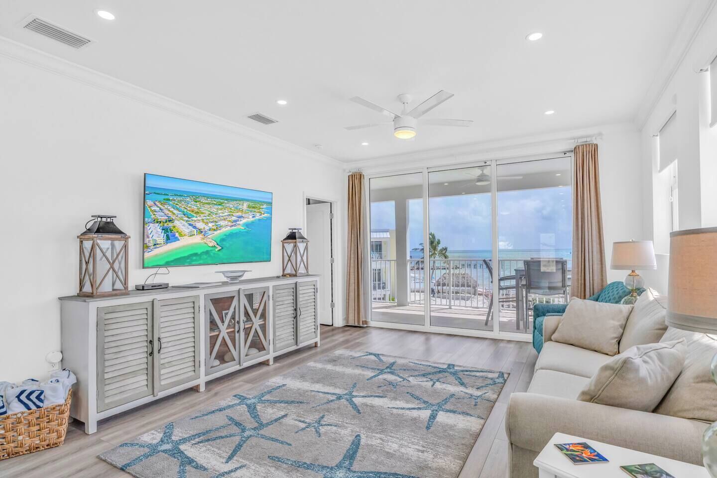 Ein modernes Wohnzimmer mit großem Fernseher, einem Balkon mit Blick auf den Strand und einer gemütlichen Sitzecke.