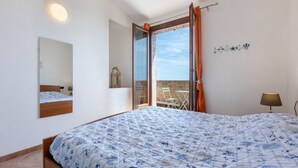Een slaapkamer met een bed, een raam met gordijnen, een nachtkastje, een lamp en uitzicht op buiten.