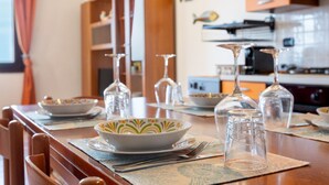 Een eettafel gedekt met servies en een schaal, houten stoelen en een keuken op de achtergrond.