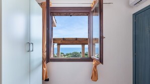 Een kamer met een raam, een houten balk, een blauwe deur en een betegelde vloer.