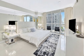 Een moderne hotelkamer met een groot bed, een televisie, een bureau en een balkon met uitzicht op de stad.