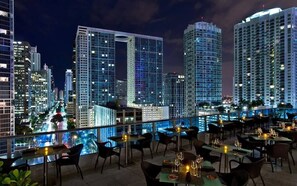 A rooftop restaurant with tables and chairs, overlooking a cityscape with high-rise buildings. - Icon Brickell 20th Floor 1BR | Pool View (Miami)
