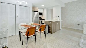 A modern kitchen with a microwave, stove, and sink. There is a dining area with a glass table and chairs. - Chic 2BR Edgewater Condo w/ Views + Balcony (Miami)