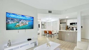 A modern living room with a flat-screen TV, a white entertainment unit, and a glass coffee table. - Chic 2BR Edgewater Condo w/ Views + Balcony (Miami)