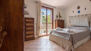 A bedroom with a bed, a wooden dresser, a wardrobe, and a balcony with a view. - GuestHost - Cozy 55 sqm apartment, ideal for 3 people, located on the first floor of a building without a lift.The property is located in San Pantaleo, a charming village in the hinterland of the Costa Smeralda, which combines the authentic charm of loca (San Pantaleo)