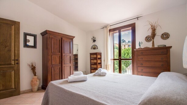 A bedroom with a bed, wooden wardrobe, and a window with a view. - GuestHost - Cozy 55 sqm apartment, ideal for 3 people, located on the first floor of a building without a lift.The property is located in San Pantaleo, a charming village in the hinterland of the Costa Smeralda, which combines the authentic charm of loca (San Pantaleo)
