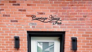 Edificio de ladrillo con una puerta blanca, dos macetas y un letrero sobre la puerta que dice "Carriage House Inn".